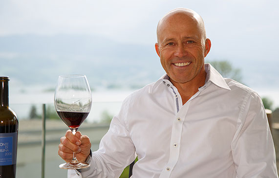 Thomas Tschirky auf einer Terrasse in einem Skigebiet, mit einem Weinglas in der Hand.